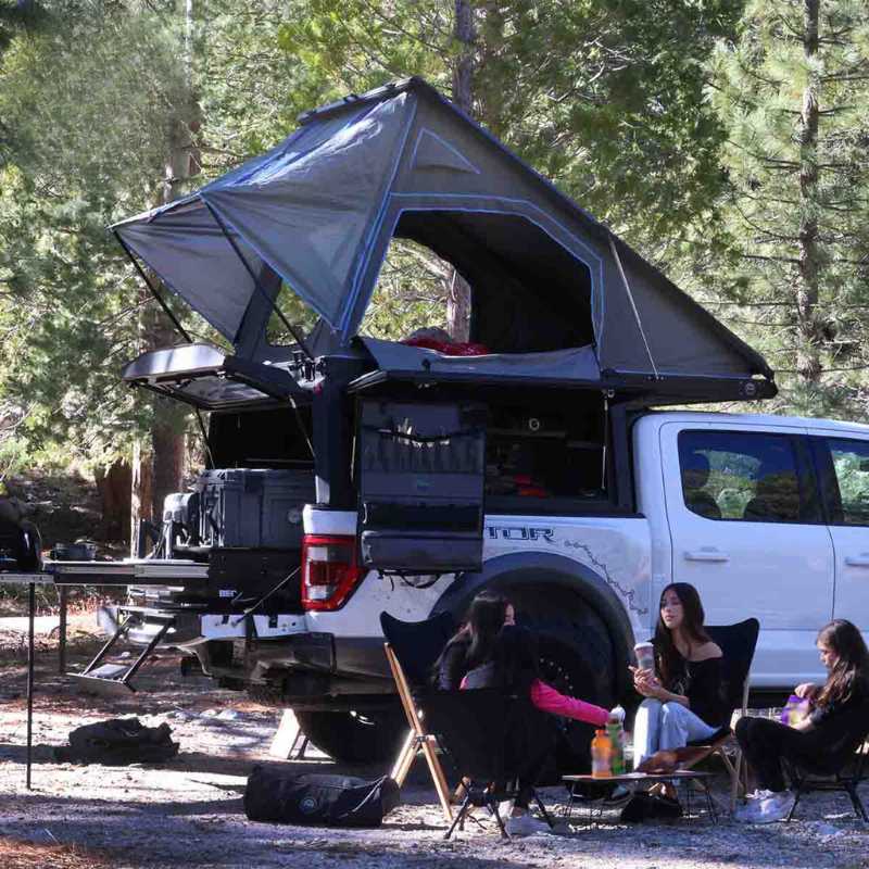 overland-vehicle-systems-magpak-camper-shell-roof-top-tent-for-jeep-gladiator-open-rear-corner-view-on-vehicle-with-people-in-nature