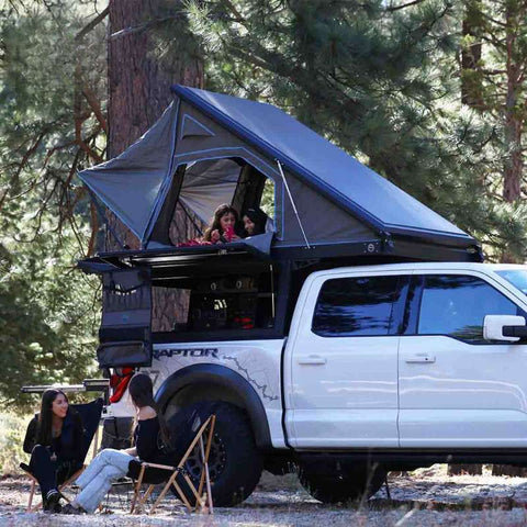 overland-vehicle-systems-magpak-truck-camper-for-ford-raptor-open-front-corner-view-with-family-camping-in-forest