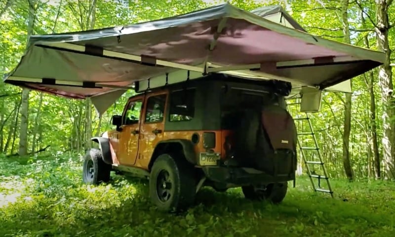 overland-vehicle-systems-nomadic-270-awning-driverside-open-rear-corner-view-on-jeep-wrangler-in-forest