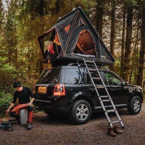 tentbox-cargo-hard-shell-roof-top-tent-open-rear-corner-view-on-land-rover-freelander-in-forest-with-persons-camping