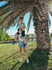 Two children next to a palm tree in front of a large sandy beach in Portugal.