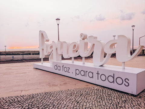 Figueira da Foz, para todos, sign in front of the clocktower and beach with sun setting on the horizon. Praia de Relogio Portugal.