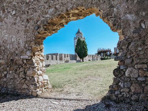 View through a hole in the castle walls of Castelo de Montemor-o-Velho framing a tree and tower