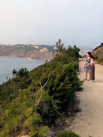 Mom and daughter on a dirt path overlooking greenery and the ocean 