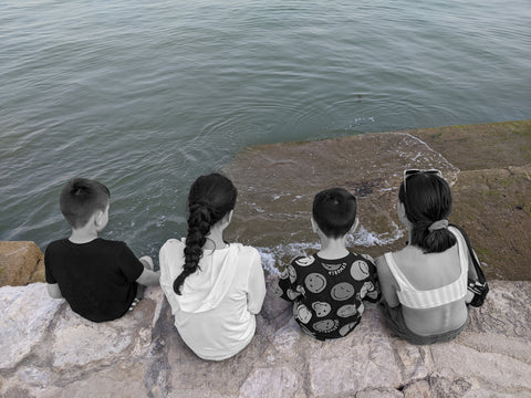 Four children sitting on a stone wall overlooking a tranquil sea