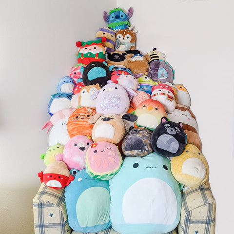 A mountain of squishmallow stuffed toys piled high on top of a chair.