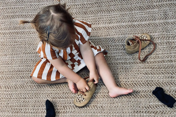 petite fille sur tapis qui enfile chaussures à lacets