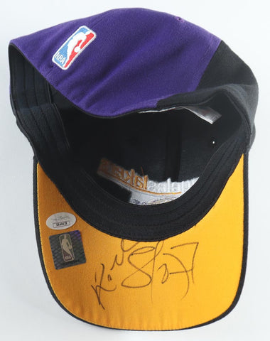 Close-up view of a Los Angeles Lakers fitted hat, adorned with the unique signatures of Kobe Bryant and Lamar Odom. The hat's bold purple color serves as a testament to Lakers' pride and is further emphasized by the official James Spence Authentication (JSA) hologram, certifying its authenticity