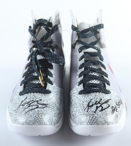 Pair of Nike Hyperdunk basketball shoes signed and inscribed by Kobe Bryant displayed in a custom case, accompanied by an official Panini hologram and Certificate of Authenticity. The size 14 shoes, reminiscent of the athletic prowess of the late basketball legend, currently stand as a sought-after item on auction