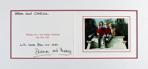 A photograph of a Christmas card, hand-signed by Princess Diana and Prince Charles III. The card, showing slight signs of age, contains their autographs in bold ink, making the signatures clearly visible. The Beckett Authentication Services hologram is visible at the bottom of the card, testifying to its authenticity