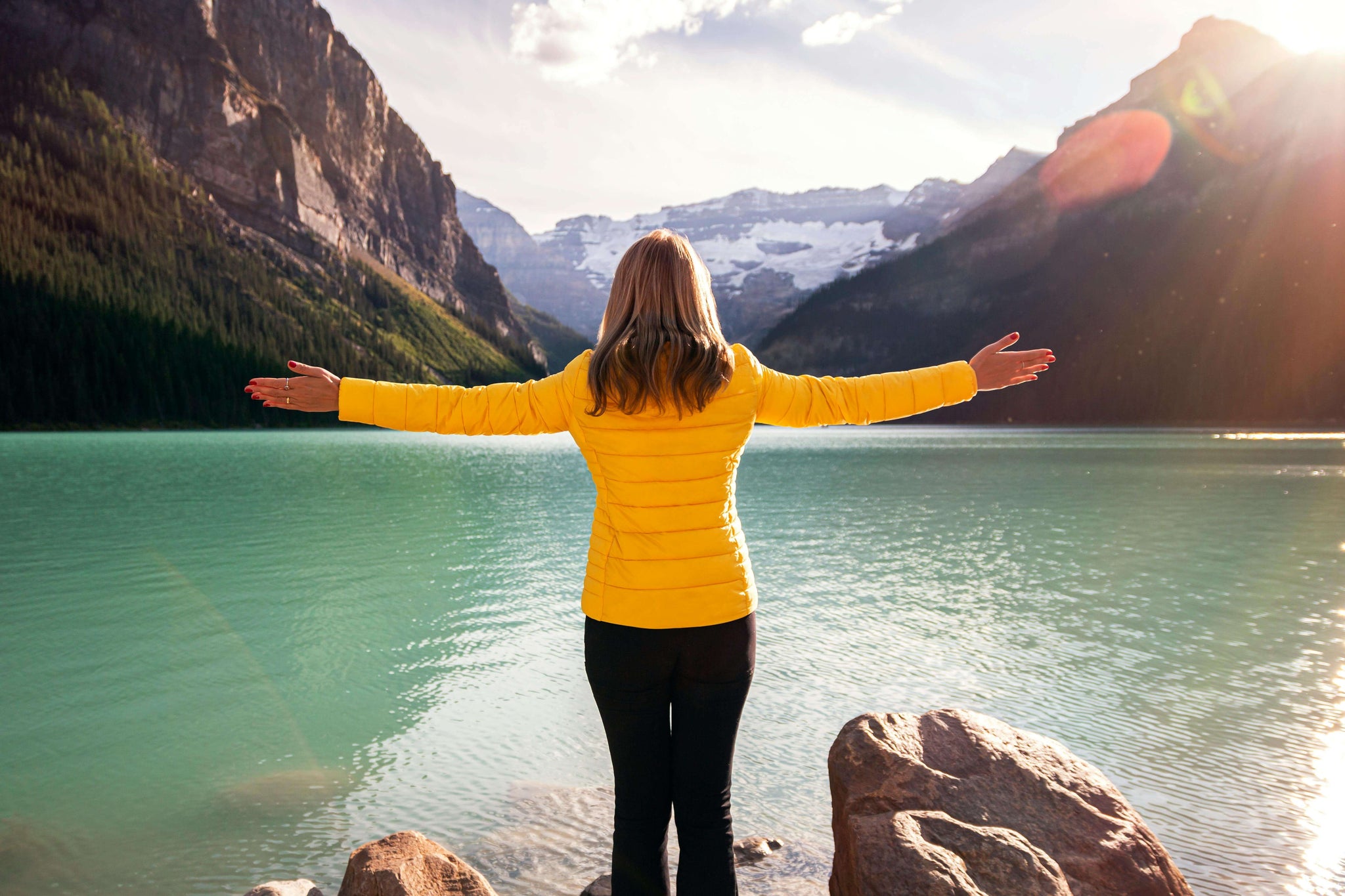 Alberta woman with a yellow jacket standing in front of a lake with her arms outstreched