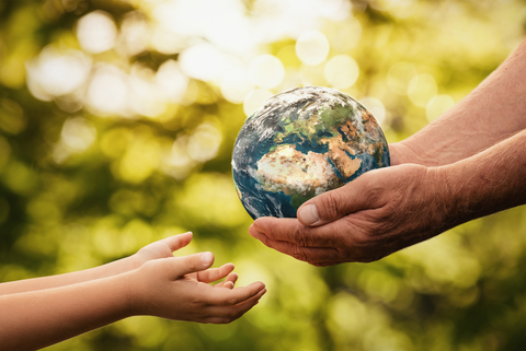 Image on green background showing a pair of adult hands passing a model of the planet earth into a child's hands