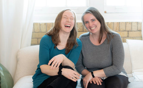 Jesi and Sam of Canary Kids Club laughing while sitting on a white couch