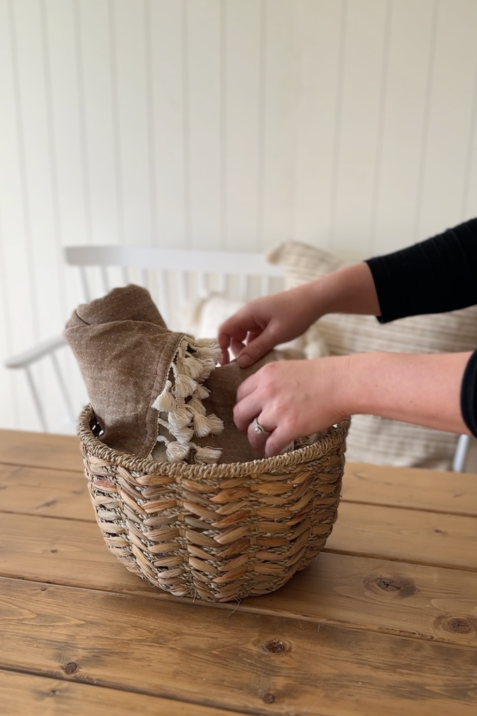 Hands placing brown muslin throw into cozy themed gift basket