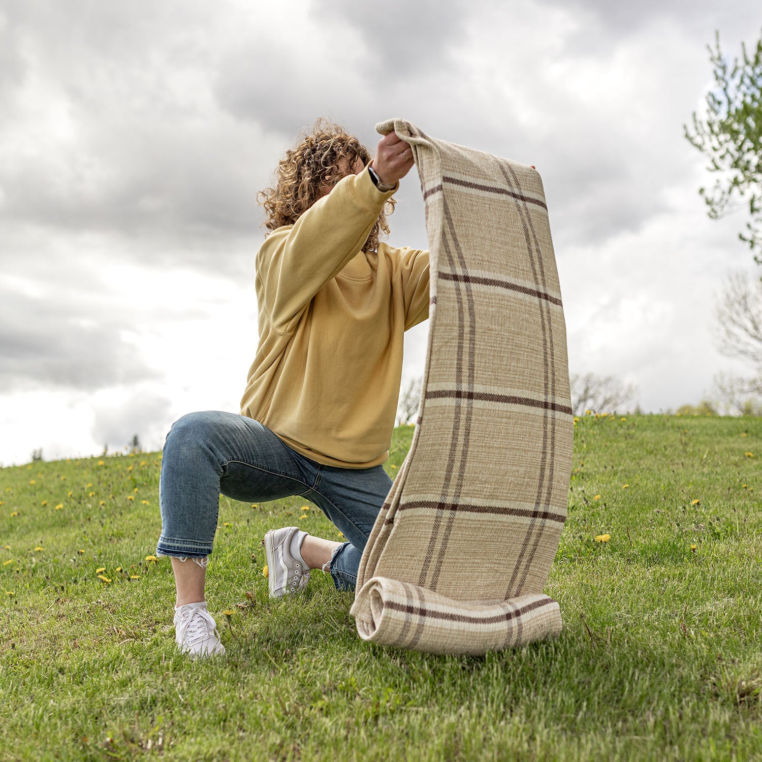 Mel brown plaid picnic blanket being laid out on grassy hillside