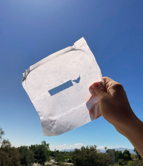Cloth with a hole shaped like the Pursuit of Knowledge logo in front of a blue sky.