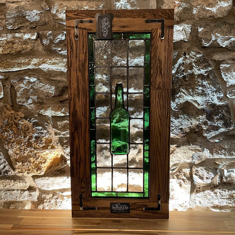 A front view of a traditional frames stained glass panel incorporating a proper-12 whiskey bottle cut in half with an oak frame.
