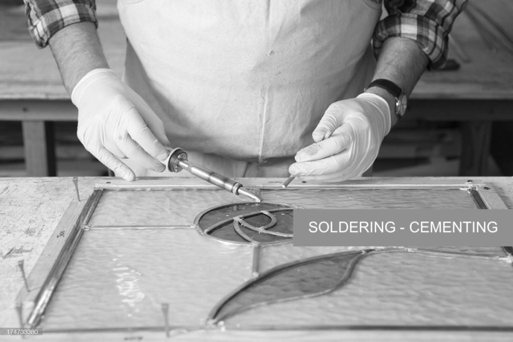 Gent soldering a pice of stained glass on a bench