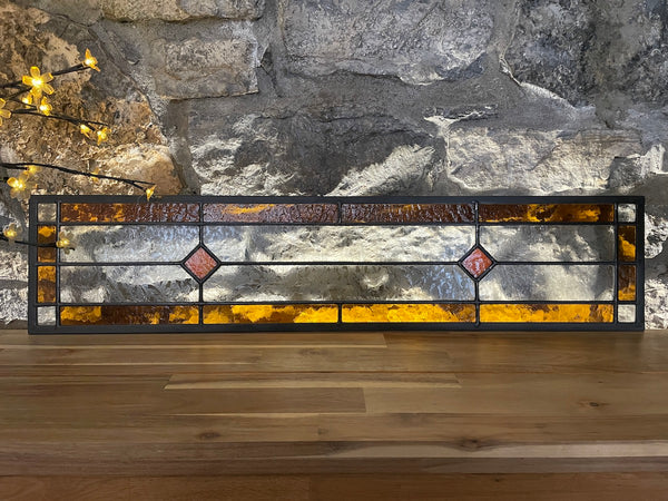 A long Amber highlighted stained glass panel shown on a bench, upright and backlit.