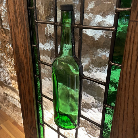 A right hand view of a traditional frames stained glass panel incorporating a proper-12 whiskey bottle cut in half with an oak frame.