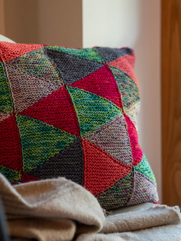 An hand knitted cushion made of triangular shaped little sections like a quilted cushion