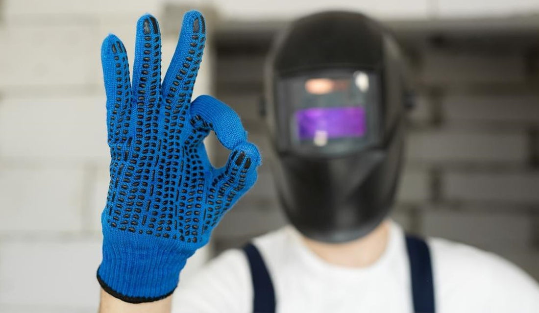 worker wearing protective welding helmet and work gloves giving okay sign