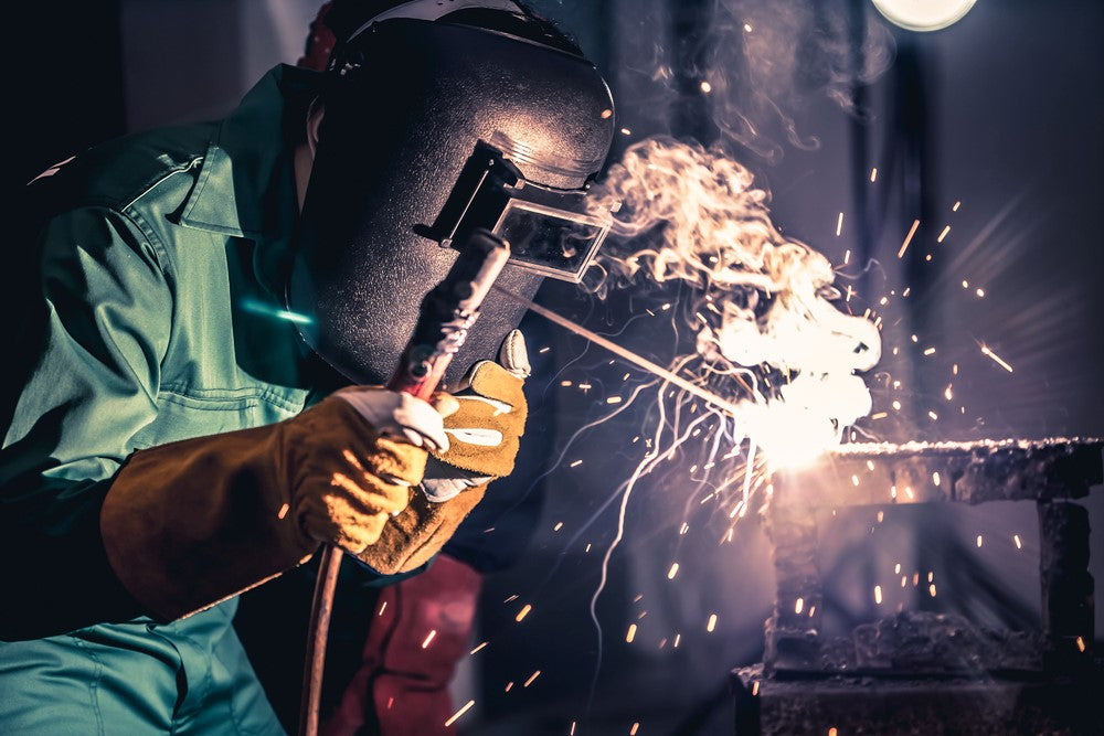 Person in welding helmet and safety gloves welding using welding rod