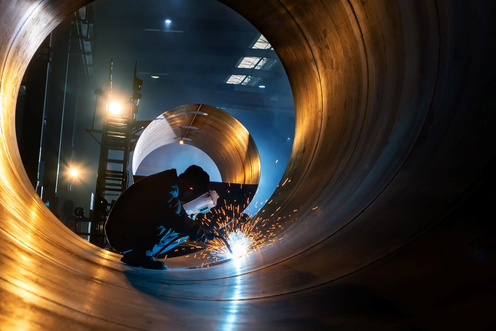 Person welding in large metal pipe with sparks flying