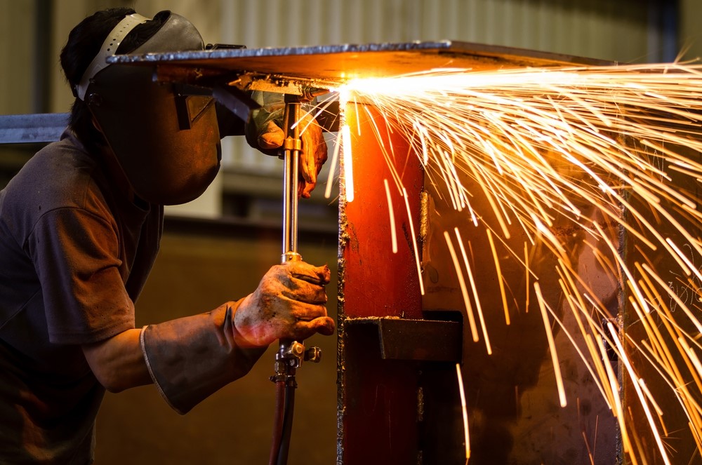 Welder in safety gear using cutting torch with sparks in workshop