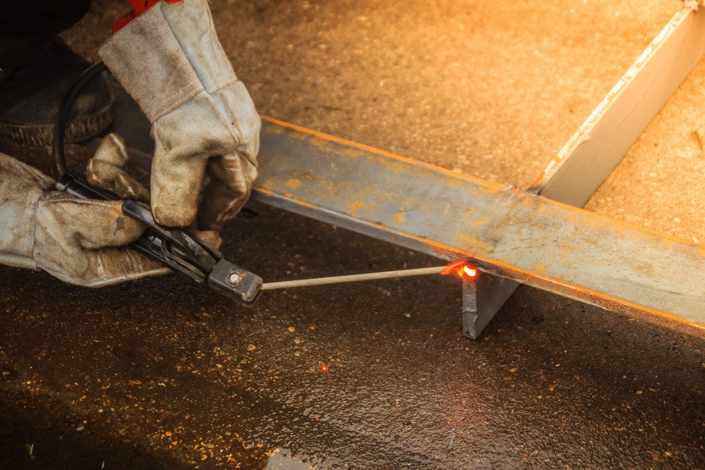 Welder in safety gloves using 7018 welding rod on metal joint