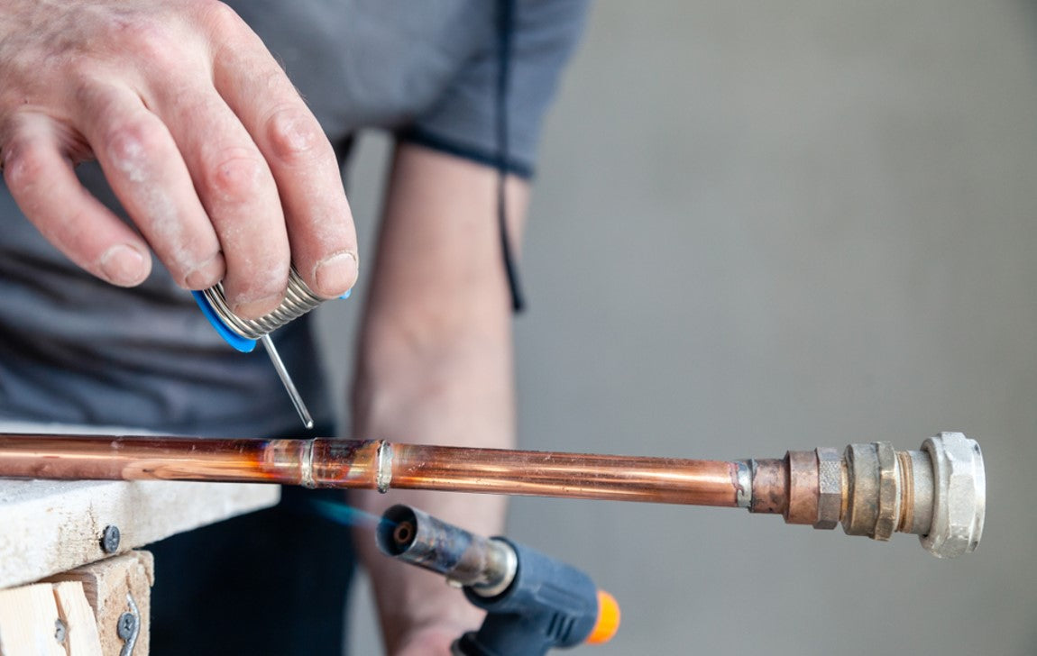 plumber carefully welding copper pipe joint with blue flame blow torch