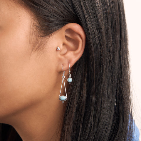 An image of an ear with 3 sterling silver earrings, 2 are Larimar stone earrings. 