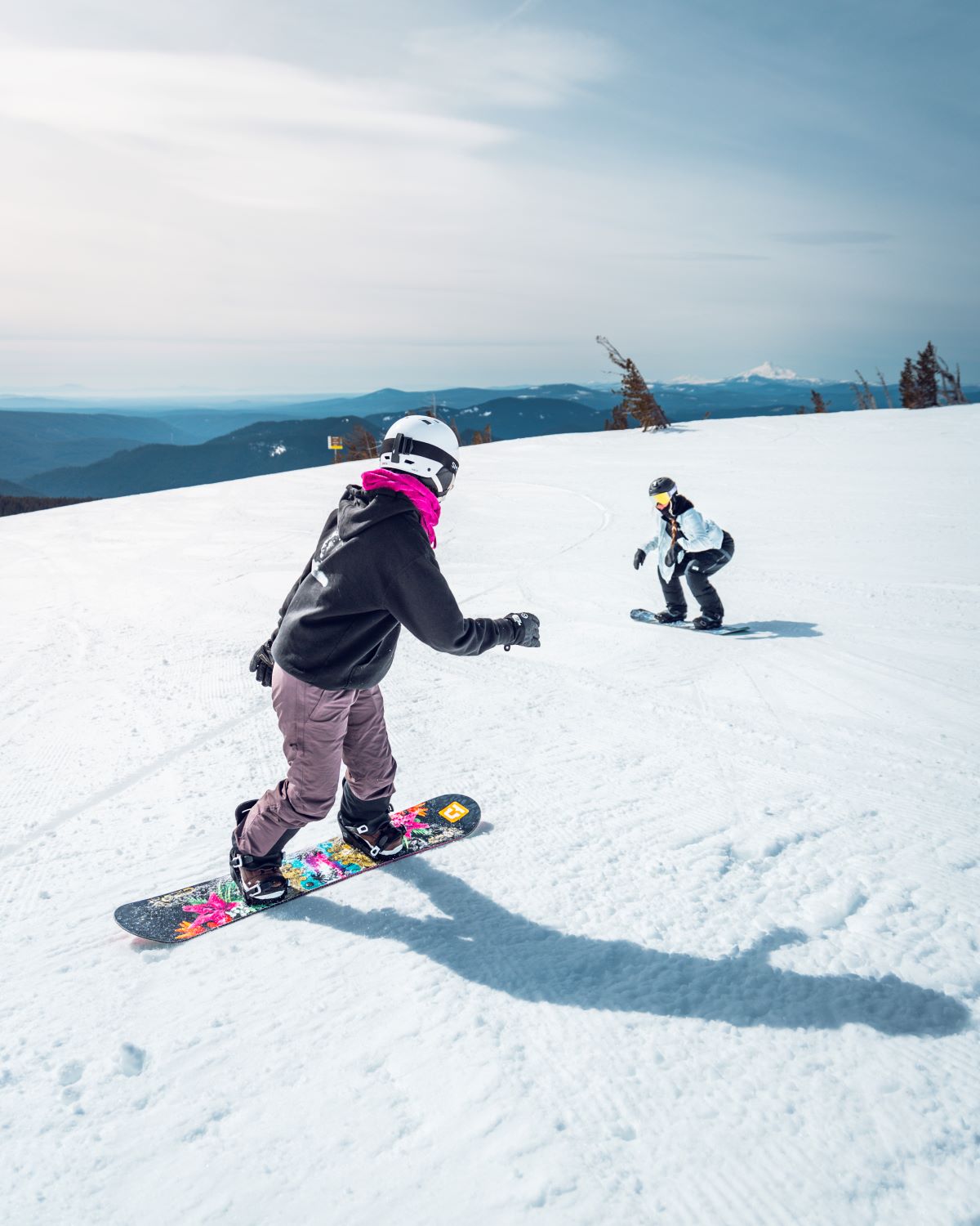 two people snowboarding down a slope both in helmets
