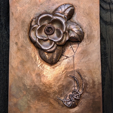 A raised copper sculpture of a camellia flower with a black widow.