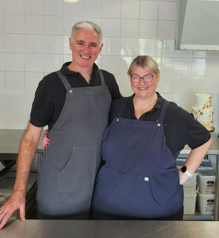 Couple standing in commercial kitchen with blue and grey aprons on