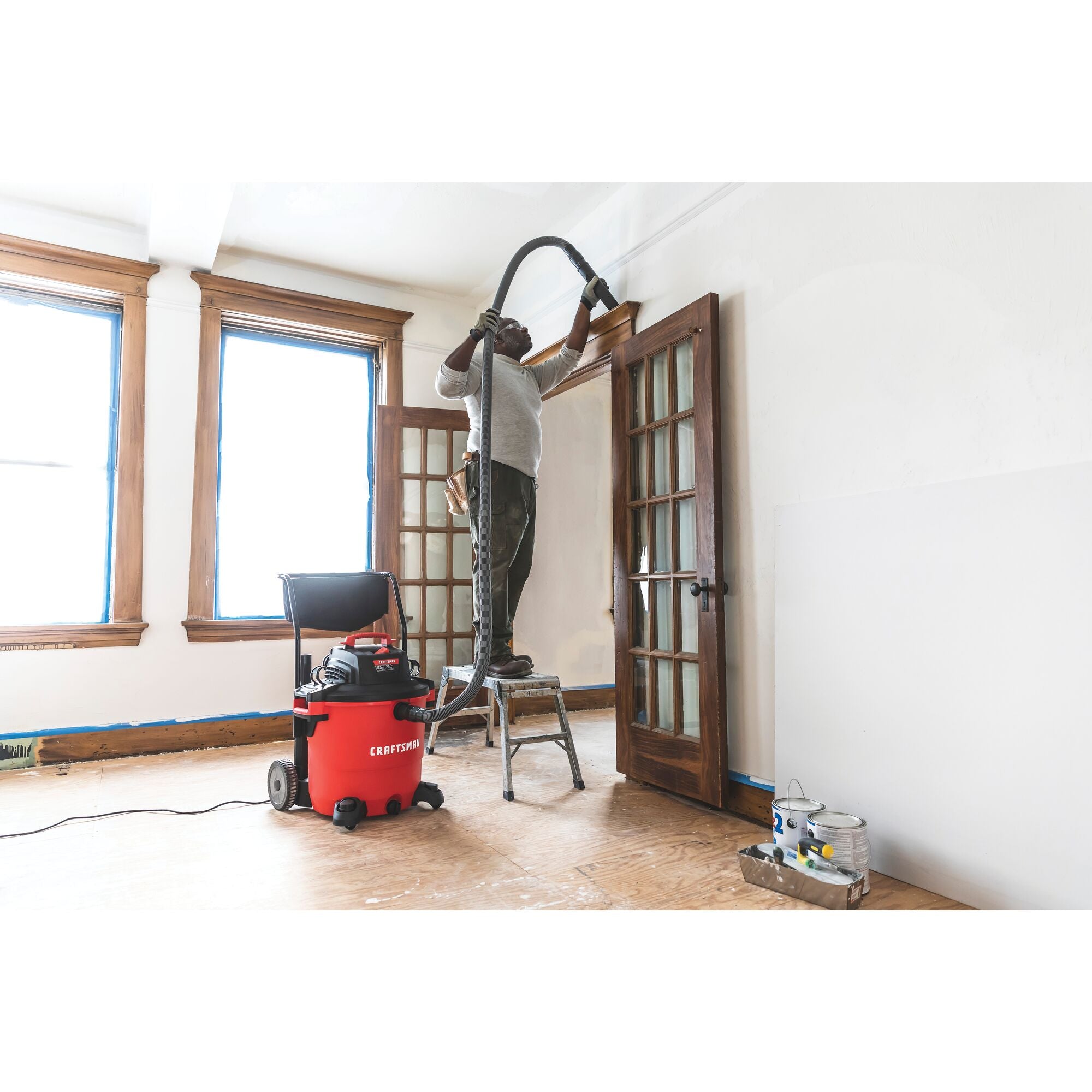 20 gallon 6.5 H P wet dry vacuum with cart being used by a person to clean wooden door frame.