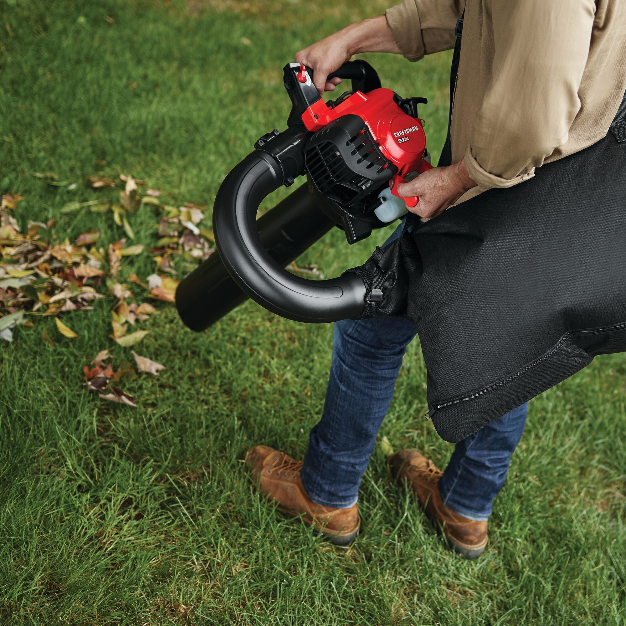 2 cycle full crank engine gas leaf blower vacuum being used by a person to remove leaves from the yard.
