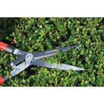 Hedge shears with compound action blade being used by a person to trim a hedge outdoors.