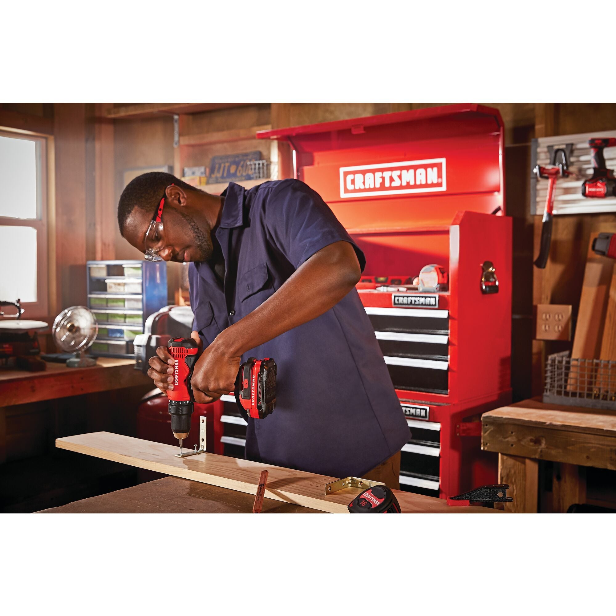 Half inch cordless drill and driver kit 2 batteries being used for fixing metal hook on wooden plank by person.