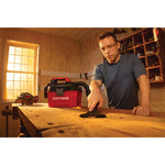 20 volt cordless 2 gallon wet dry vacuum being used by a person to clean wooden work station.