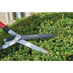 Hedge shears with compound action blade being used by a person to trim a hedge outdoors.