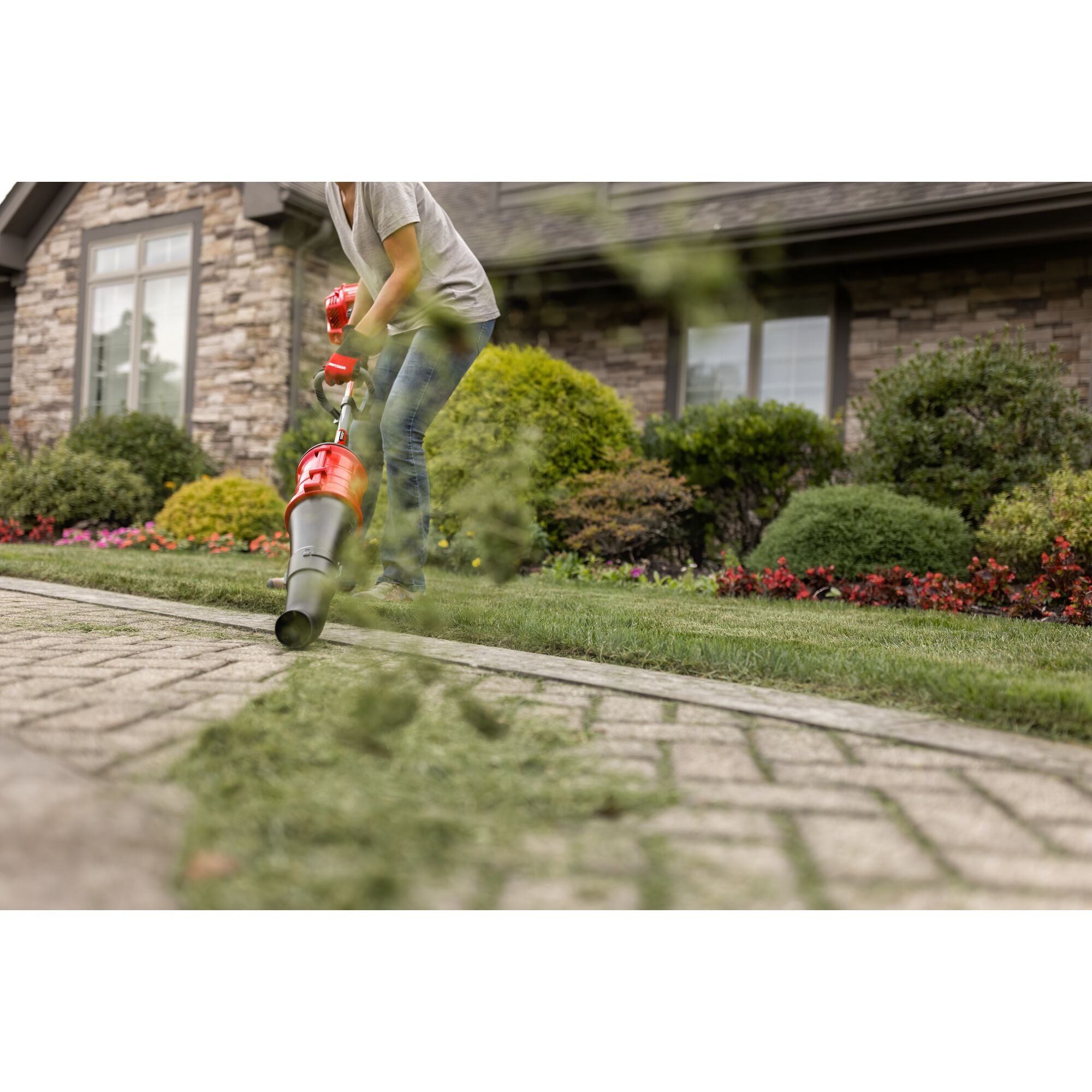 CRAFTSMAN cone blower attachment head blowing grass off sidewalk in front of a house in gray shirt and jeans