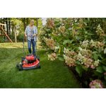 CRAFTSMAN M100 140cc Push Mower mowing near flower bed with bushes wearing jeans and plaid button up shirt