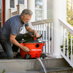 Man kneeled down on porch with CRAFTSMAN 12 Gallon Vac draining water from drum through drain
