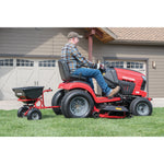 85 pounds tow broadcast spreader being used to spread fertilizer in lawn by person.