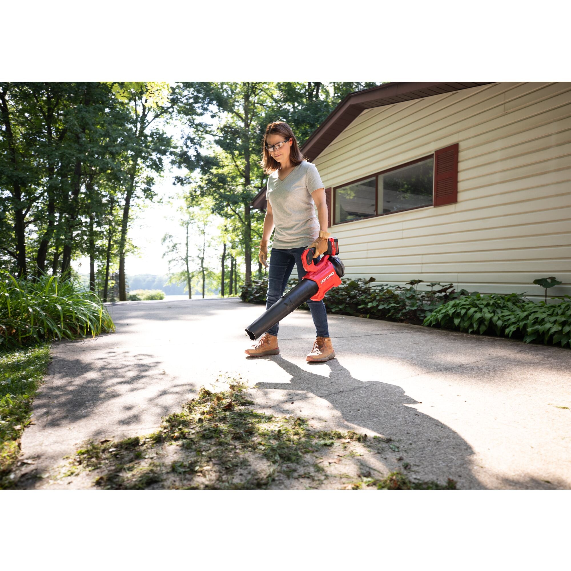 CRAFTSMAN V20 BRUSHLESSRP Blower clearing grass off driveway home in background