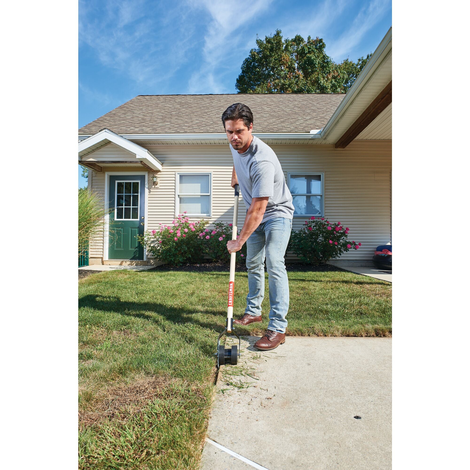 Wood handle edger being used by a person to make a clean edge against the pavement.