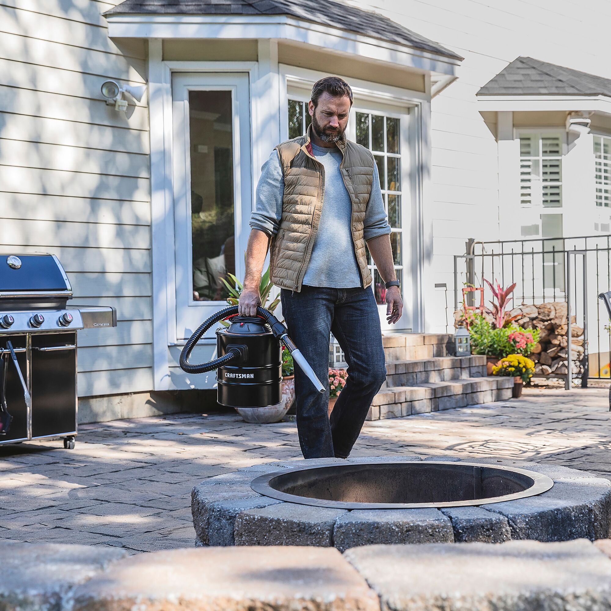 Man carrying CRAFTSMAN 5 gallon ash vacuum and accessories to outside fire pit to clean