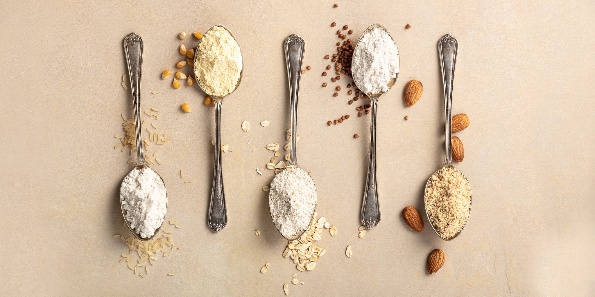Five metal spoons with different types of gluten-free flour.