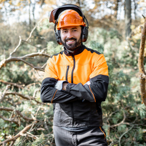 Professional lumberjack smiling confidently in protective gear while working in the forest, surrounded by trees and natural scenery during his forestry job